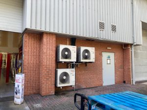 Bank of three wall-mounted commercial air conditioning condenser units on a brick elevation, typical R410A plant at a UK commercial premises