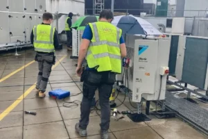 AKS Air Conditioning engineers in high-visibility clothing servicing rooftop air conditioning plant in wet weather
